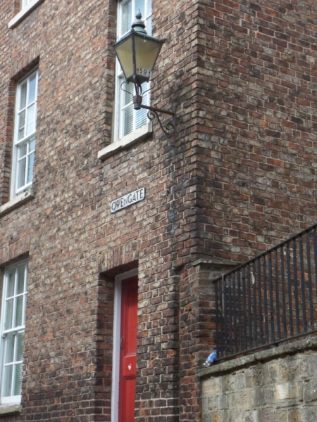 A street corner with an old-fashioned gas lamp, a red door and a sign reading Owengate