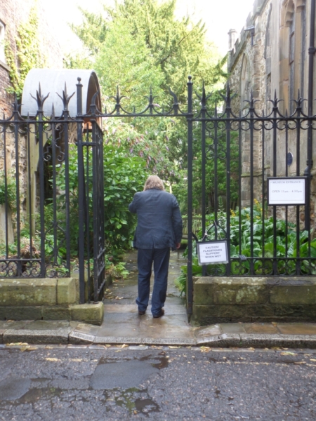 The back of a person in a suit, standing in wrought-iron gate leading to a garden